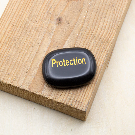 Piedra de los deseos de obsidiana negra con la palabra PROTECTION grabada en dorado.